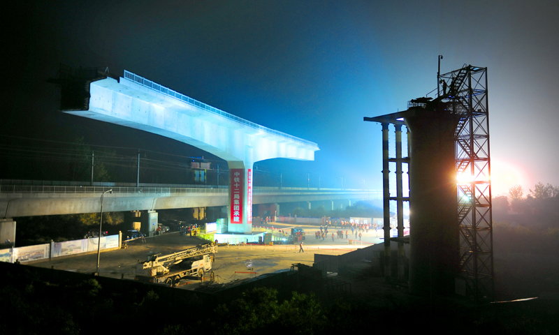 徐（州）鹽（城）鐵路，自西向東橫貫江蘇北部，被譽為江蘇腹地的“鐵路金腰帶”，與京滬、隴海、滬通等鐵路相通相連。此次轉體施工的跨京滬高鐵特大橋集跨運營線、鄰既有線施工于一體，是全線控制性工程。圖為轉體前的梁體。