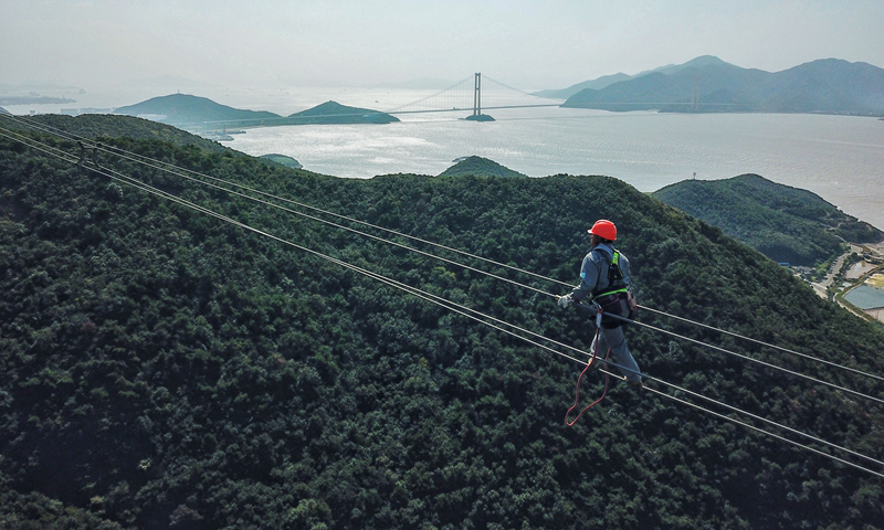 檢修消缺工作的完成將進一步提高舟山聯網輸電線路的運行可靠性，保障舟山群島安全可靠用電。圖為10月24日，檢修人員在跨海輸電高塔上進行走線工作。（新華社記者 徐昱 攝）