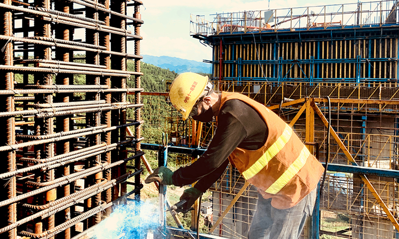 入夏以來，該項目通過交流座談等形式，第一時間解決高溫下堅守崗位、辛勤工作的一線工人防暑降溫需求，聽取施工一線人員的建議。圖為烈日下的一線工人在百米墩身頂部焊接鋼筋。（馬奇 攝）