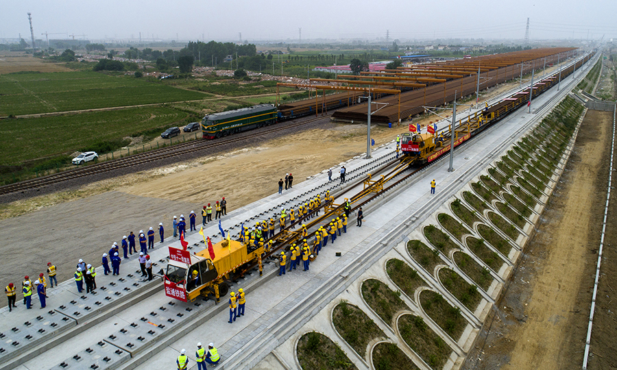 6月12日，在江蘇省東臺市的鹽通高鐵東臺站外施工現場，中國鐵建所屬中鐵十一局鋪軌機牽引著第一組500米長鋼軌平穩地落在無砟道床上，標志著我國“八縱八橫”高鐵網沿海通道重要組成部分的鹽通高鐵建設整體從線下施工轉入線上軌道鋪設階段。圖為鹽通高鐵全線首鋪現場。（劉連強 攝）