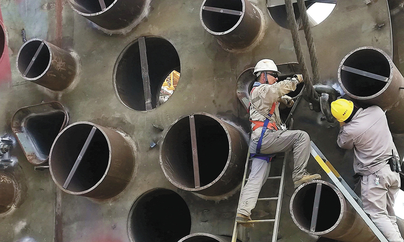 5月15日，海西灣畔，中國海油所屬海洋石油工程股份有限公司青島場地碼頭，一座身著嶄新紅藍外衣的“鋼鐵巨城”靜靜漂浮在輕霧繚繞的海面上。圖為作業人員安裝吊裝鎖具。