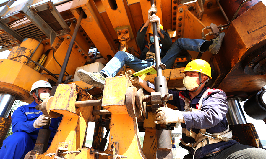 據了解，架梁施工是該項目復工的關鍵點，直接影響后續鋪軌施工的開展。在嚴格落實防疫工作的基礎上，該項目部組建4人故障排查小隊，確保復工后設備安全運轉，并加強人員培訓教育，以“試卷+提問”方式考核合格后方能上崗。自2月28日復工后，該項目在運距5.5公里基礎上以日均1榀箱梁的進度有序推進，后續將按施工組織設計增加二個鋪架作業口，全力推進施工進度。圖為施工人員調整架橋機支腿。（蔡如錦 攝）