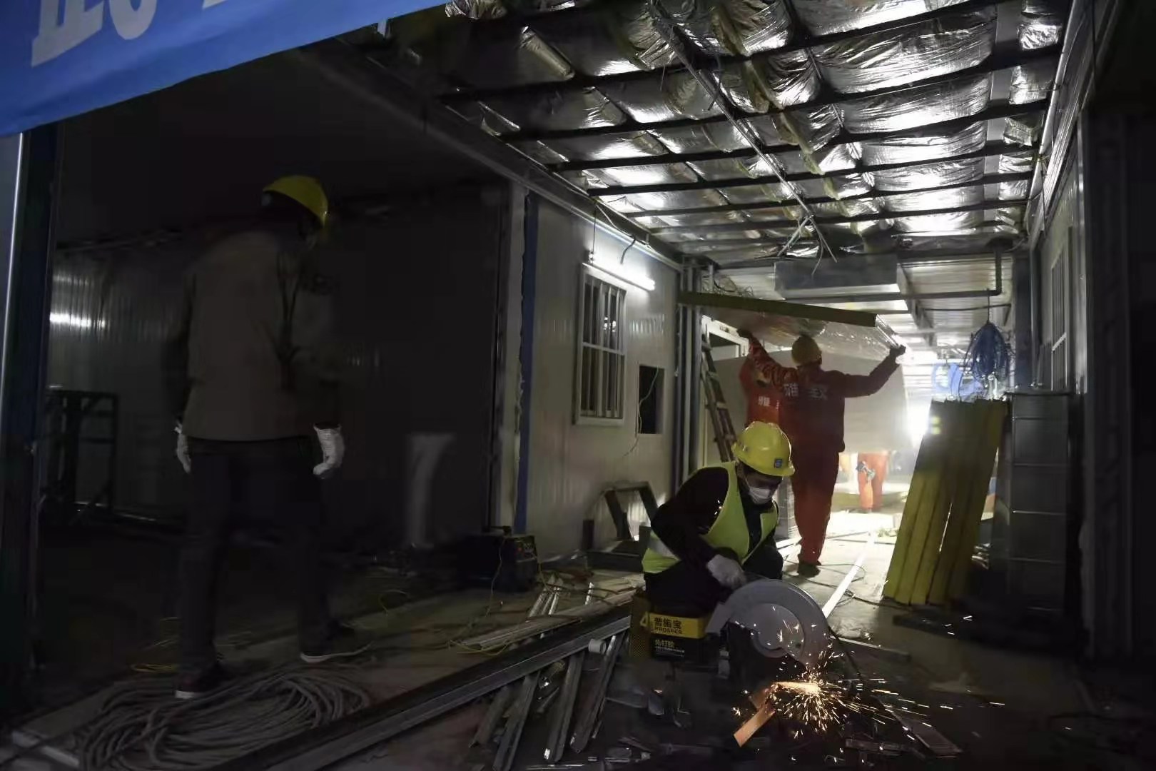 為了優質高效地推進火神山醫院項目實施，1月25日項目啟動之時，中建三局現場成立了6支、322名員工組成的青年突擊隊，青年員工們紛紛請戰，并且從全國各地“逆行”馳援武漢參戰。為保證施工進度，青年突擊隊制定了“小時制”作戰地圖，搭建了工程“大數據”，并采取24小時輪班作業，突擊隊員不畏疫情兇險，精誠團結、通力合作，很多人不眠不休沖鋒在施工一線。圖為2月1日17時30分，火神山醫院一號樓，施工人員在進行室內裝潢。