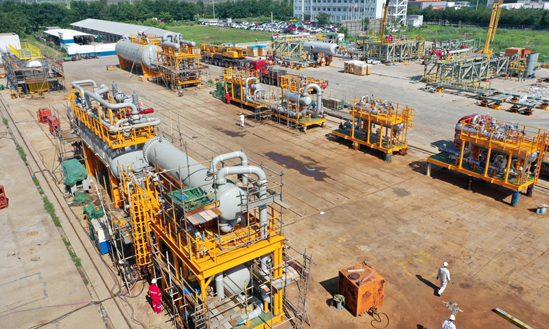 8月15日，中國海油所屬海油工程特種設備分公司臨港場地迎來今年最壯觀的一天，10多臺套即將集中交付的橇裝設備，整齊地排成兩條鋼鐵長龍，猶如受閱部隊等待檢閱。叉車、運輸車、汽車吊穿梭其間，巨大的龍門吊來回奔走，將一臺臺設備搬運到小火車一般的長拖運輸車上。圖為作業現場。