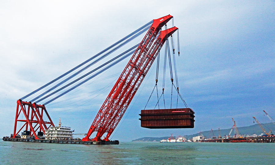 施工中，項目組相繼對“埋植式”平臺搭建技術、海上樁基施工技術、鋼吊箱快速施工技術等方面展開研究。他們采用的兩項核心技術為世界首創，參與研制的我國首座臺風區雙孔連做造橋機獲得國家發明專利。圖為首個千噸級主墩鋼吊箱運輸吊放。
