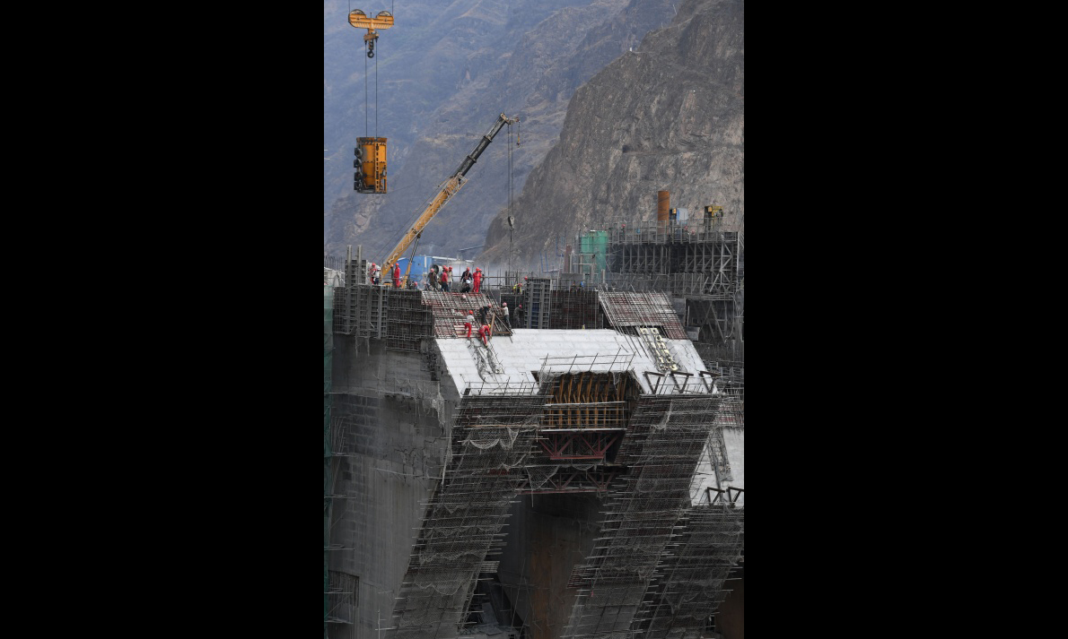 中國能建葛洲壩集團共承擔了烏東德工程13個標段施工任務，約占烏東德水電站主體施工任務的75%。目前，大壩工程、左岸地下電站、泄洪洞三大標段正處于緊張的施工高峰期。電站計劃于2020年7月下閘蓄水、8月首臺機組發電，2021年12月全部機組投產發電。圖為5月30日，建設中的烏東德水電站大壩主體工程。（新華社記者 陳曄華 攝）