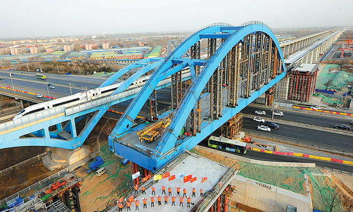 春節期間，由中國鐵建所屬中鐵十二局承建的京雄城際鐵路黃固村特大橋跨京開高速公路一體式雙線簡支鋼箱拱橋頂推順利完成。該橋跨度為114 米，重達3100 噸，是京雄鐵路全線重點控制性工程。在歷時7天的頂推施工中，中鐵十二局制定了“毫厘監控，穩健頂推”等嚴謹的安全措施，確保了春運期間京開高速公路安全暢通。（賈鵬翼 攝）