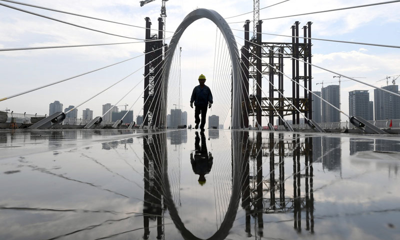 據了解，白沙大橋主塔最高點達106米，為空間異形結構，仿佛將兩根筆直的鋼塔在空中擰成一個“麻花”，是目前世界上最高、跨度最大的“反對稱結構斜拉橋”。圖為5月29日，一名工人從建設中的柳州白沙大橋上經過。新華社發（黎寒池 攝）