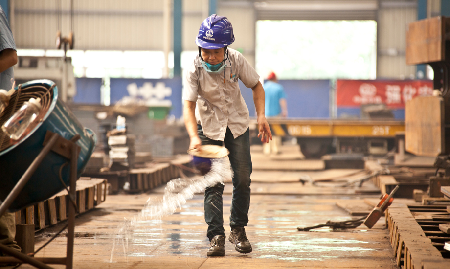 盡管室外氣溫已達38攝氏度，因為安全防護需要，中鐵四局鋼結構建筑公司制造分公司的作業工人也必須把自己從頭到腳防護起來。汗水從帽子和眼鏡的縫隙里流淌下來。每個工位都有不停轉的風扇，每個工人都有超大容量的水杯。每年他們都要經歷百十來個這樣難熬的高溫工作日。（作者：朱曉晨）
