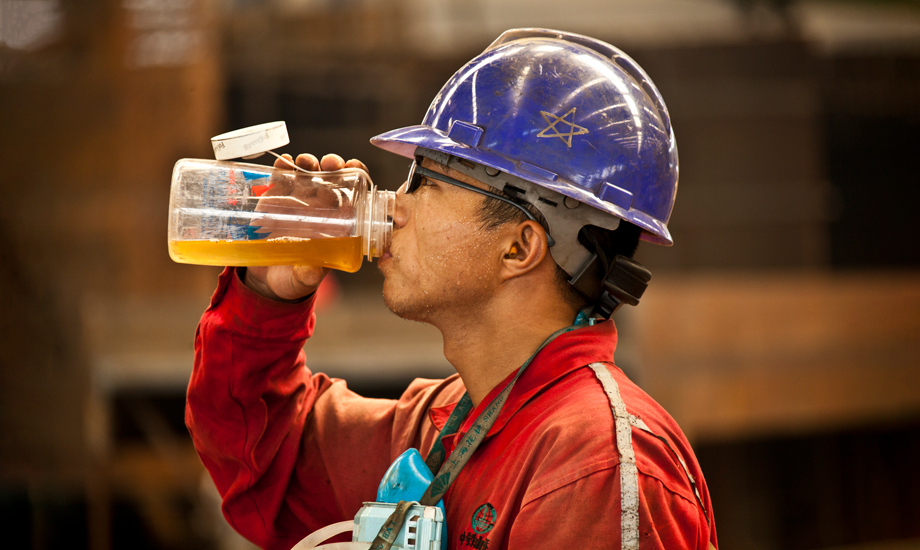 盡管室外氣溫已達38攝氏度，因為安全防護需要，中鐵四局鋼結構建筑公司制造分公司的作業工人也必須把自己從頭到腳防護起來。汗水從帽子和眼鏡的縫隙里流淌下來。每個工位都有不停轉的風扇，每個工人都有超大容量的水杯。每年他們都要經歷百十來個這樣難熬的高溫工作日。（作者：朱曉晨）
