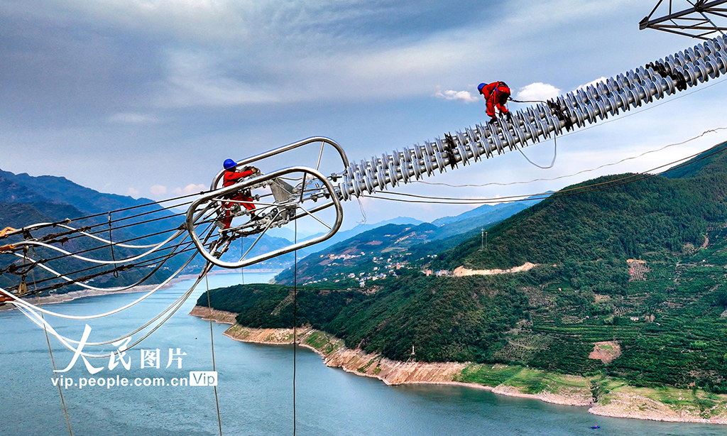 ±800千伏特高壓直流輸電線路工程白浙線，屬我國實施“西電東送”戰略的重點工程，是促進國家能源結構調整和節能減排的重大清潔能源項目。白浙線為白鶴灘水電站電力外送二期工程，起于四川省涼山州布拖縣，止于浙江省杭州市余杭區，線路全長2140.2千米。圖為2022年8月20日，湖北省恩施土家族苗族自治州巴東縣東瀼口鎮綠竹筏村，電力工人冒著40℃以上的高溫跨越長江施工作業。張遠明 攝