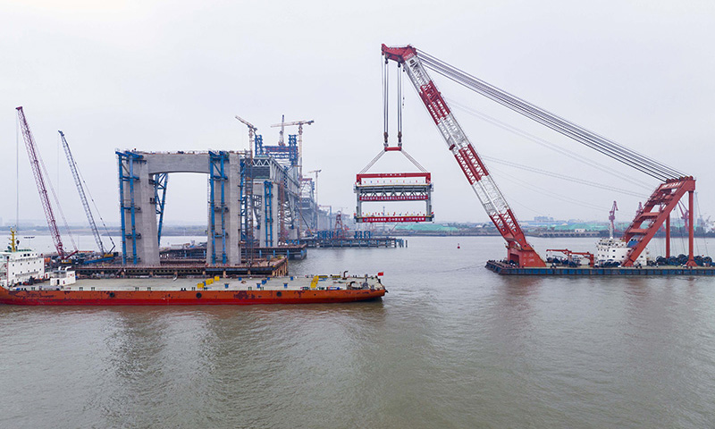 常泰長江大橋是一座公鐵兩用斜拉橋，連接江蘇省常州市與泰州市。建成后，主航道橋主跨達1176米，將成為世界上跨度最大的斜拉橋。圖為3月20日，中交二航局建設者在常泰長江大橋主航道橋泰州側施工現場進行首節段鋼桁梁架設（無人機照片）。新華社發（湯德宏 攝）