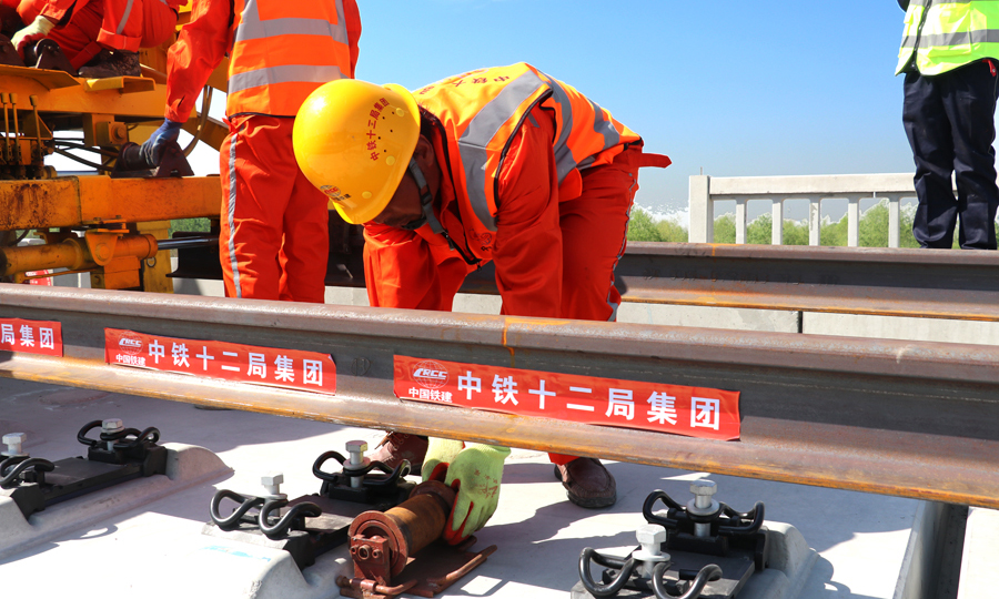 建設者在行進的機車上安裝了物理臨近報警系統，當攜帶有電子施工防護牌的現場施工作業人員進入設置的危險距離時，該系統會語音報警提示機車司機，并對現場施工防護員發出聲光報警提示。同時，項目部調度中心技術人員還在機車上安裝嵌入了國內自主研發的“北斗”定位車載定位系統，兩項技術的“聯姻”能夠保證鋪軌作業時精準定位機車行進位置，并采取在機車前后方安裝攝像頭的方式，實時傳輸線路上機車運行畫面和行駛速度，確保鋪軌作業運輸智能化、信息化。圖為安裝長軌導向輪。