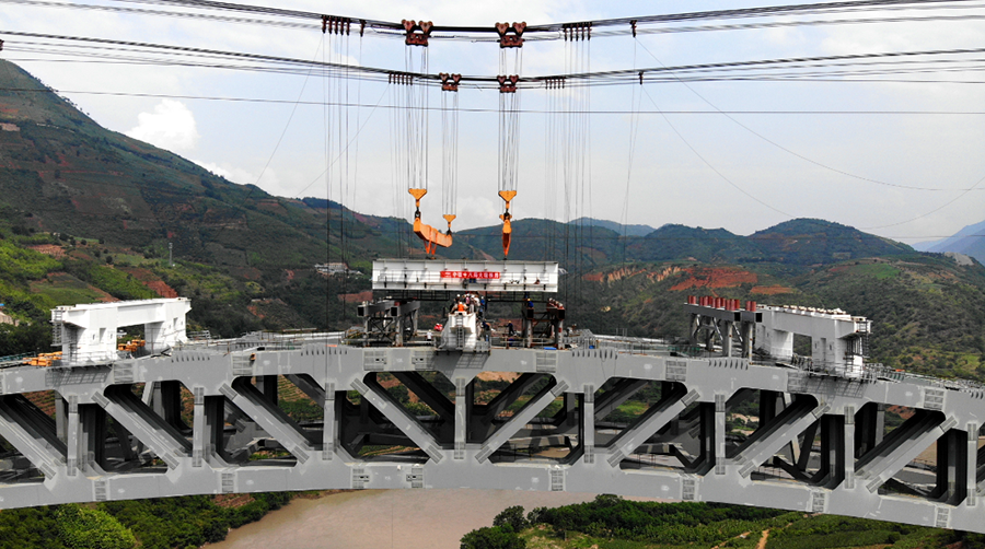 為保證大橋主拱穩定性，降低施工風險，大橋梁部施工采用“吊裝+頂推”的施工方案。拱上鋼箱梁利用纜索吊吊裝，跨中五節段鋼箱梁采用“支架法”拼裝，然后以此五節段梁體為施工平臺，進行剩余節段的焊接組裝，組裝成標準梁段后，采用纜索吊由跨中向兩側對稱吊裝，吊至相應梁位后對位焊接。隨后，借助專用焊接平臺完成鋼箱梁環縫的焊接、補涂裝施工任務，利用檢修通道完成鋼箱梁塊體之間的高強螺栓施工工作。圖為鋼箱梁節段落位。