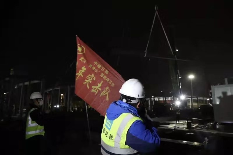 2月1日21時，火神山醫院施工現場仍是一派熱火朝天，中建三局施工人員正在挑燈夜戰，工地上施工人員24小時不眠不休，為了在2月3日交付使用全力沖刺。圖為青年突擊隊旗幟在火神山飄揚。