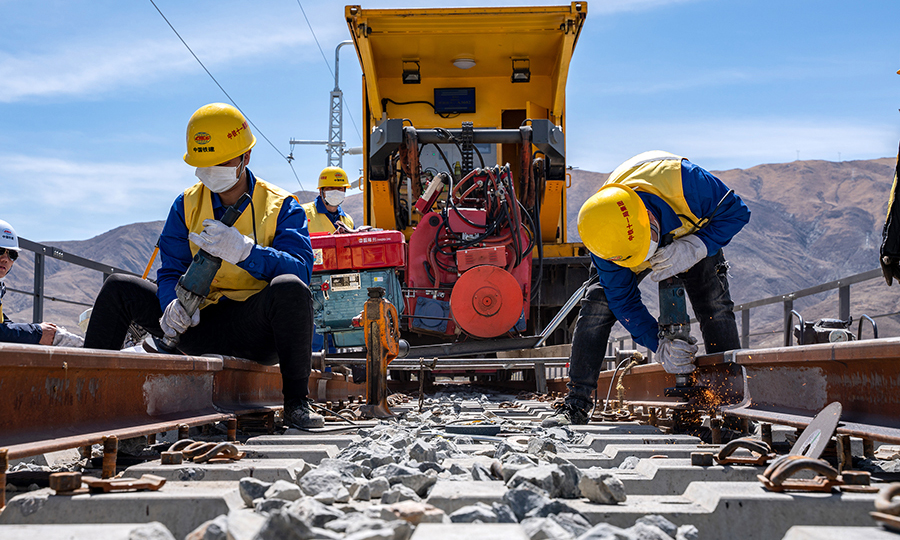作為鐵路建設中最精細、技術含量最高的工序環節之一，拉林鐵路無縫線路焊接采用了國內先進的移動閃光焊技術，鋼軌焊接經專業技術人員操作，每個焊接好的焊頭經過推凸、粗磨、焊后熱處理、外形精整、超聲波探傷，建立起獨有的“信息檔案”，檔案還包括焊接接頭記錄表，可實現質量追溯。圖為施工人員正在進行除銹工序。（丁慶濱 攝）