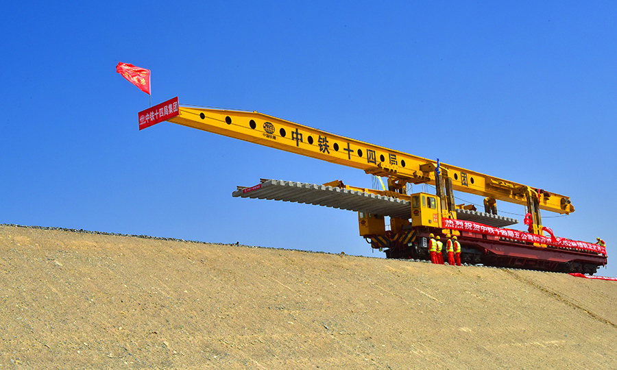 其中，中鐵十四局承擔著和若鐵路PJS2標段2312片T梁的預制、架設和535公里鋪軌等任務，鋪軌里程占全線總長的65%。沿線氣候干旱，資源匱乏，風沙天氣繁多，晝夜溫差大，穿越無人區,軌料的運輸距離也長達700多公里。項目部調集具有沙漠施工經驗的管理和施工人員，借鑒額哈鐵路建設經驗，成立課題攻關小組，科學組織，超前謀劃，采用邊臨建施工，邊組織設備進場的方案保證進度。圖為鋪軌現場。