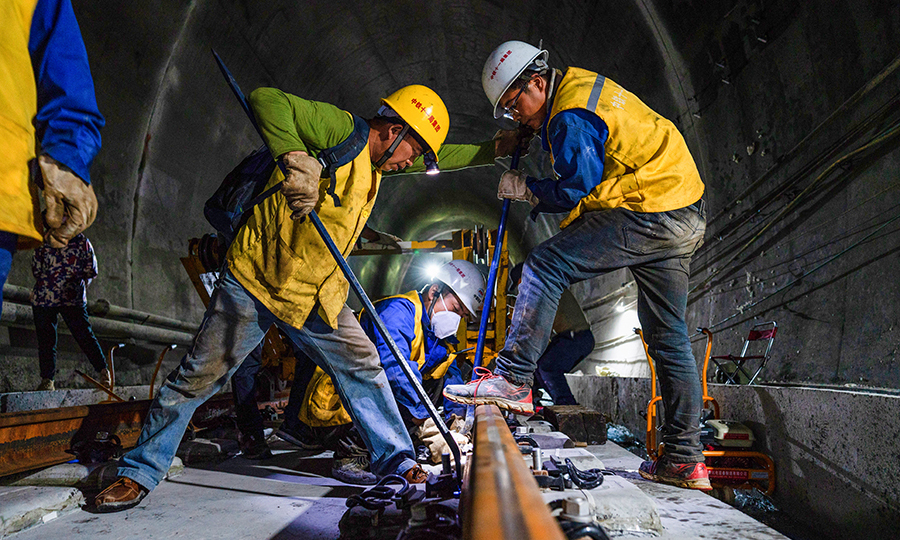 在正式鋪軌前，中國鐵建所屬中鐵十一局三公司拉林鐵路項目部通過為期兩天的機械調整、試鋪作業等準備，已經完成了有砟鋪軌1.5公里，現在采用推送法，利用WZ500長軌推送車在隧道內鋪設500米長鋼軌，后期將采用高原型DPK32鋪軌機進行有砟鋪軌，預計每天有砟鋪軌3公里。圖為現場技術員正在指導工人們調整軌距。