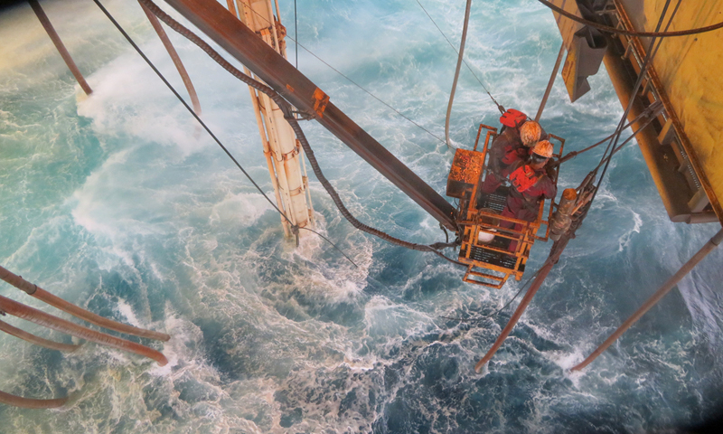 圖為“海洋石油982”鉆井平臺起防噴器作業中，員工在風浪中懸掛拆除鵝頸管，確保平臺順利起航避臺。